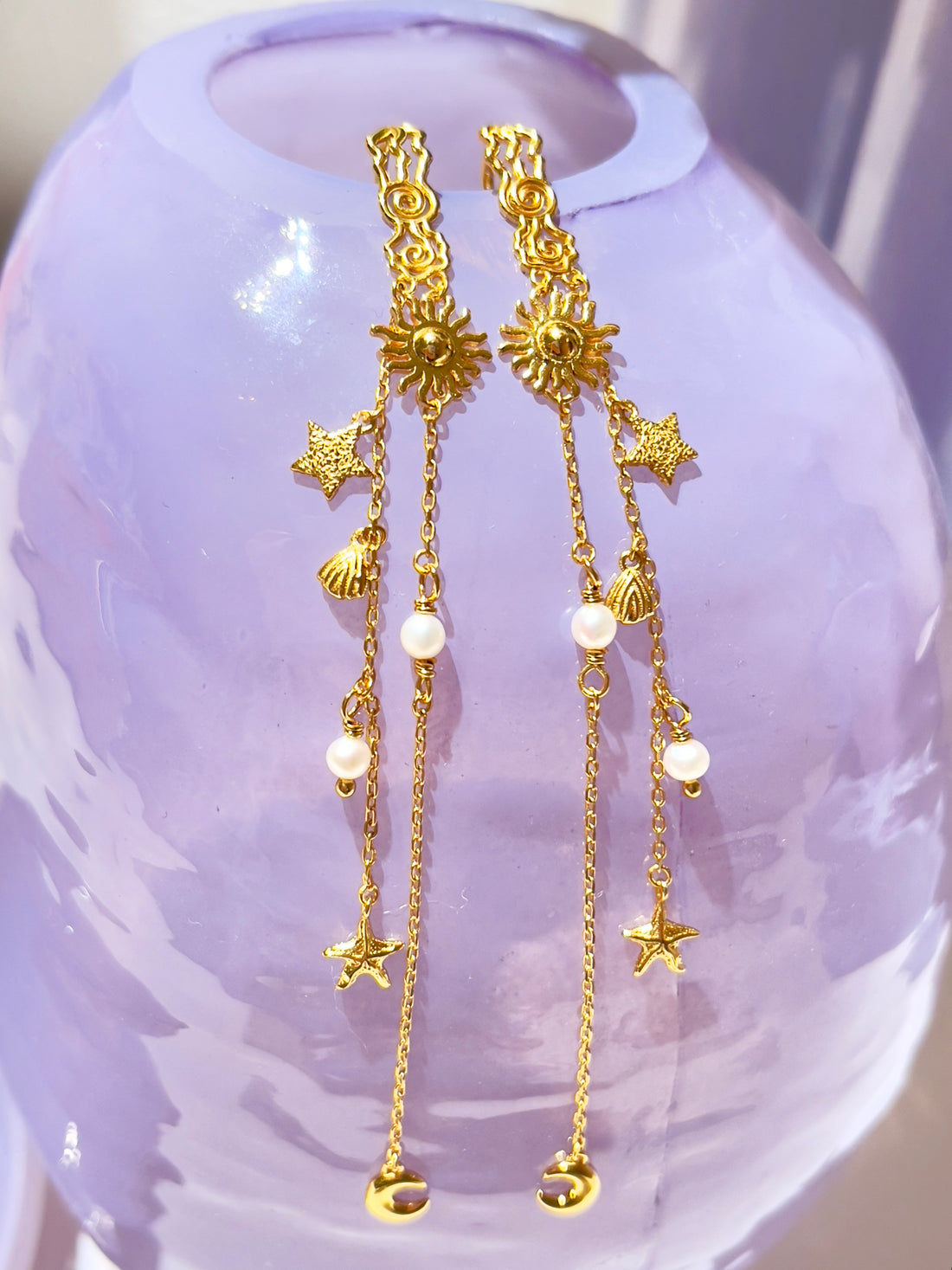 Pallantis Smykkers Ocean Dream Øreringe har guld-dangle-øreringe med sol-, stjerne-, måne-, skal- og perle charme på fine kæder i forgyldt sølv og prydet med ferskvandsperler.