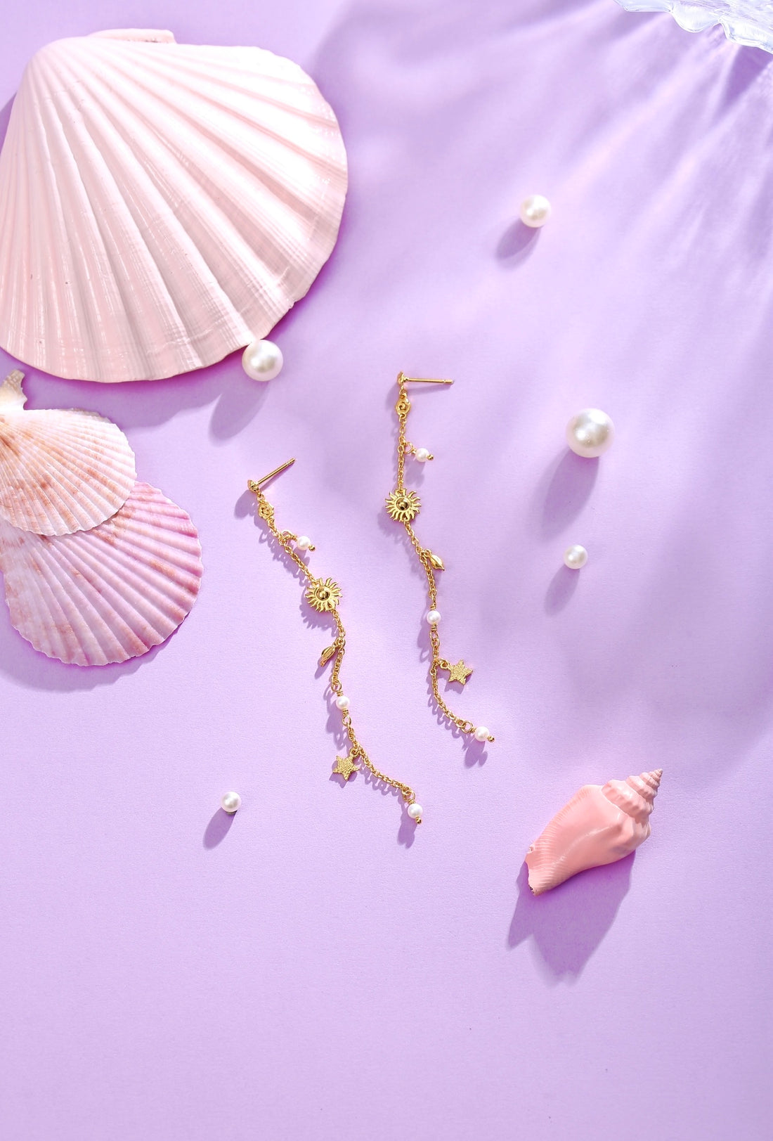 Et par lange Drømme Stjerne Øreringe fra Pallantis Smykker i forgyldt sølv med sol- og stjernevedhæng, små hvide ferskvandsperler og bladdetaljer på fine guldkæder.