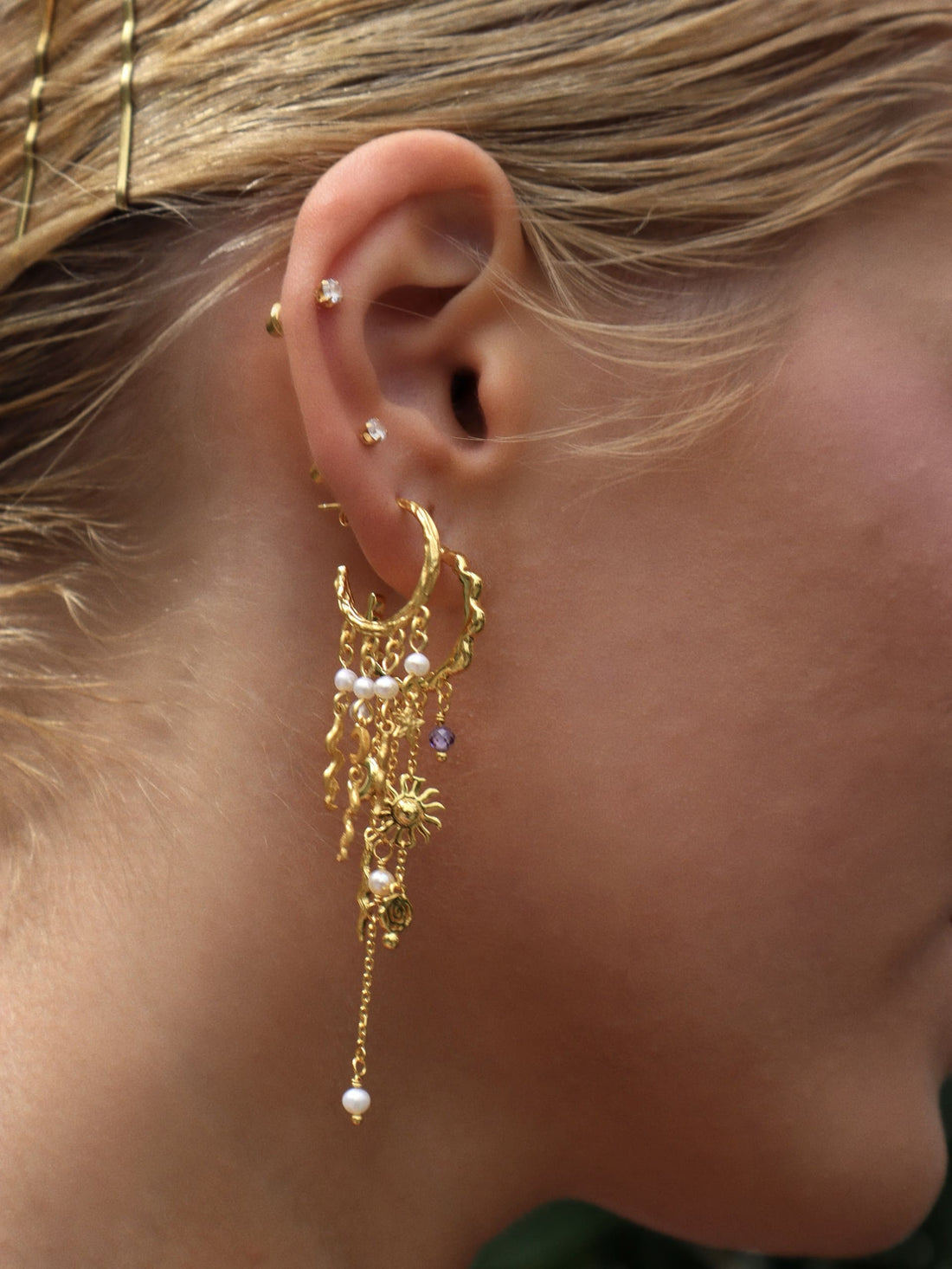 Stjernehimmel Øreringe by Pallantis har guldbøjler med dinglende bølgede linjer, halvmåner, stjerner og små hvide ferskvandsperler i et himmelsk inspireret forgyldt sølv design.